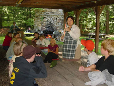 Students sitting at tables under a pavilion with teacher